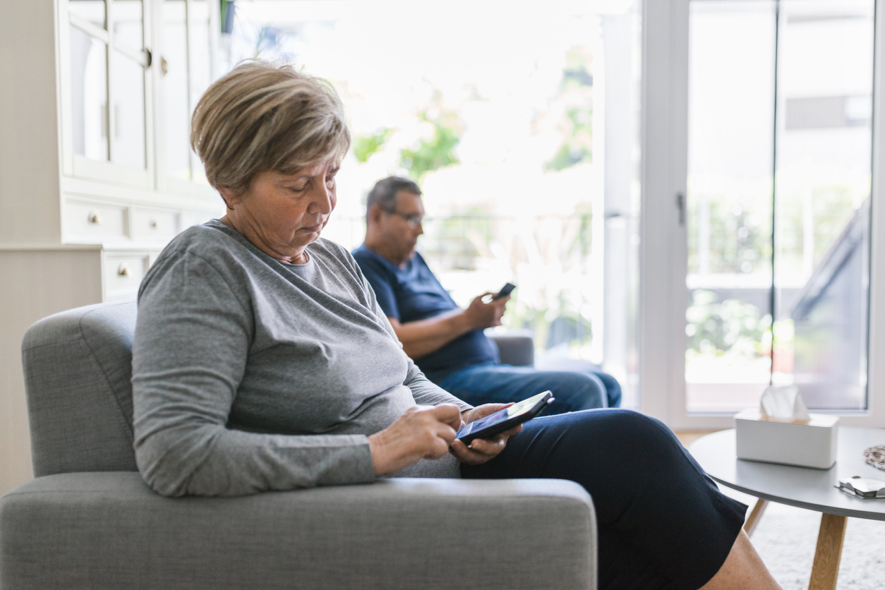 Senior couple sitting on couch and using their mobile phones at home