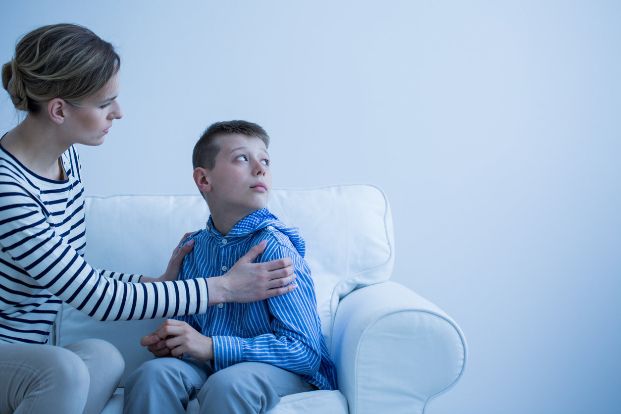 Mom in striped shirt calms her son who has panic attack while sitting on white sofa for Parental Alienation